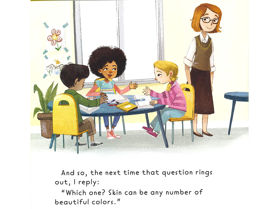 A classroom setting with three students seated around a round table having a conversation. The student in the middle with brown curly hair is speaking to a student with blonde hair next to her. A teacher stands nearby them listening to their conversation.