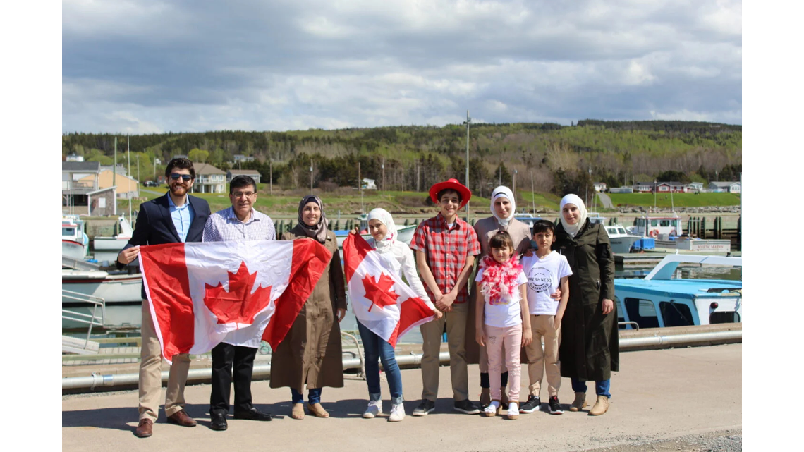 A diverse group of people holding Canadian flags and smiling.