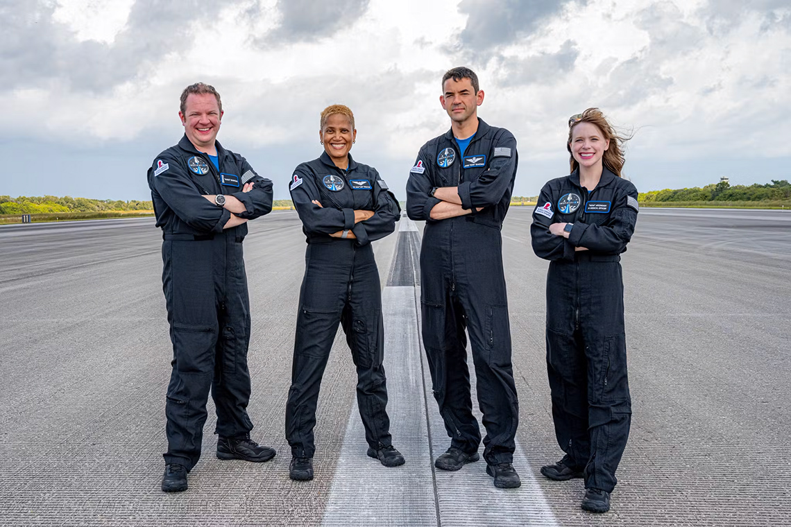 Four smiling civilians wearing flight suits