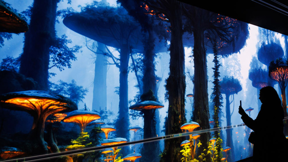 A person viewing a wall-sized digital projection of a dark forest of mushroom-shaped trees full of giant glowing mushrooms
