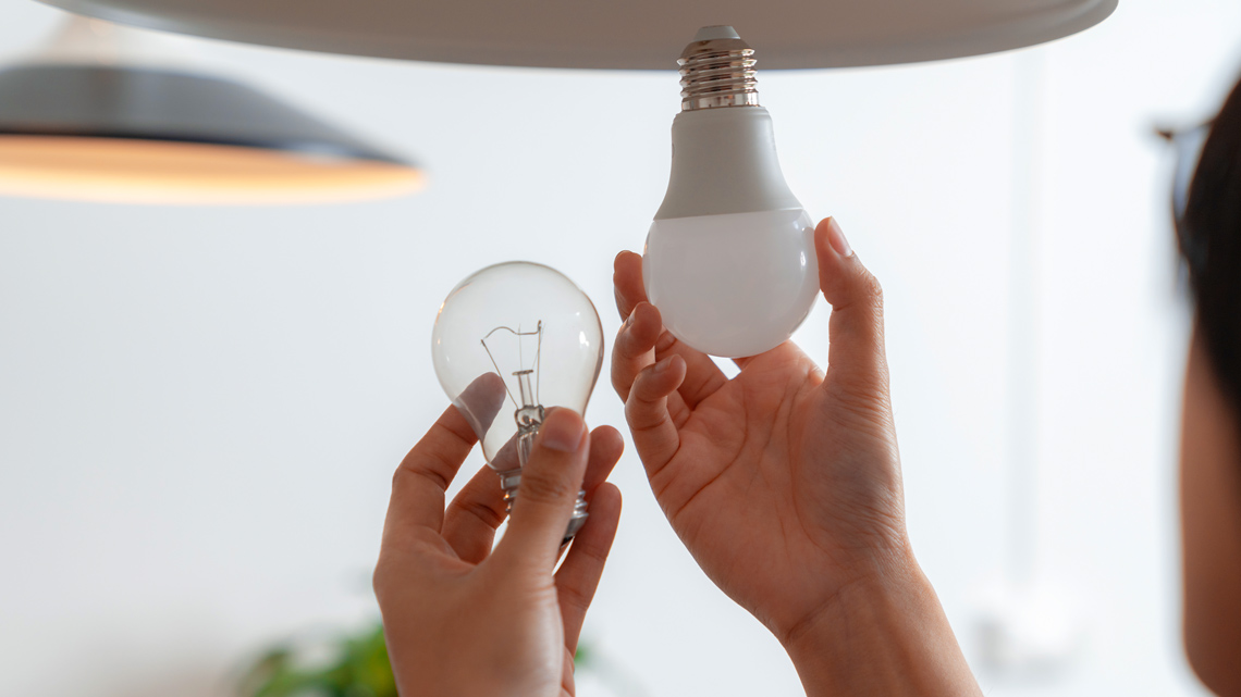 A person replacing an incandescent lightbulb with an L E D lightbulb