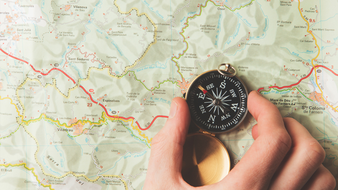 A person holding compass on top of a map