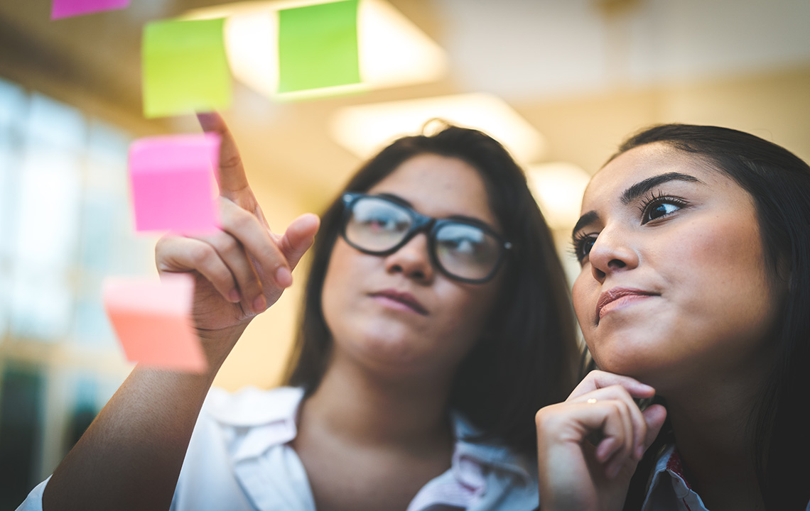 Two employees looking at posted sticky notes.