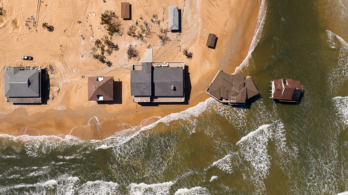 Drone view of several houses on the beach and some are in the water because the coast has eroded.