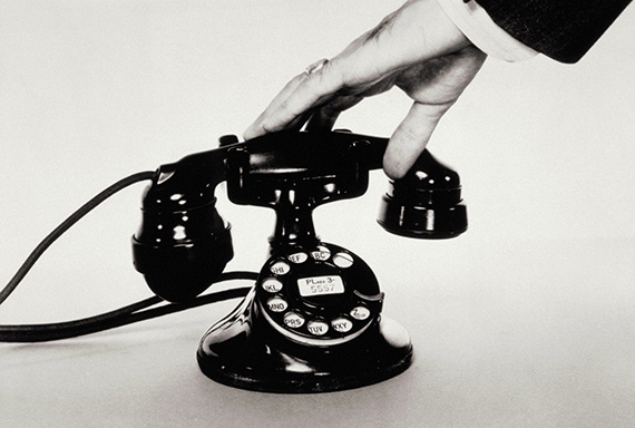 A hand grabbing the receiver of an old rotary dial telephone.