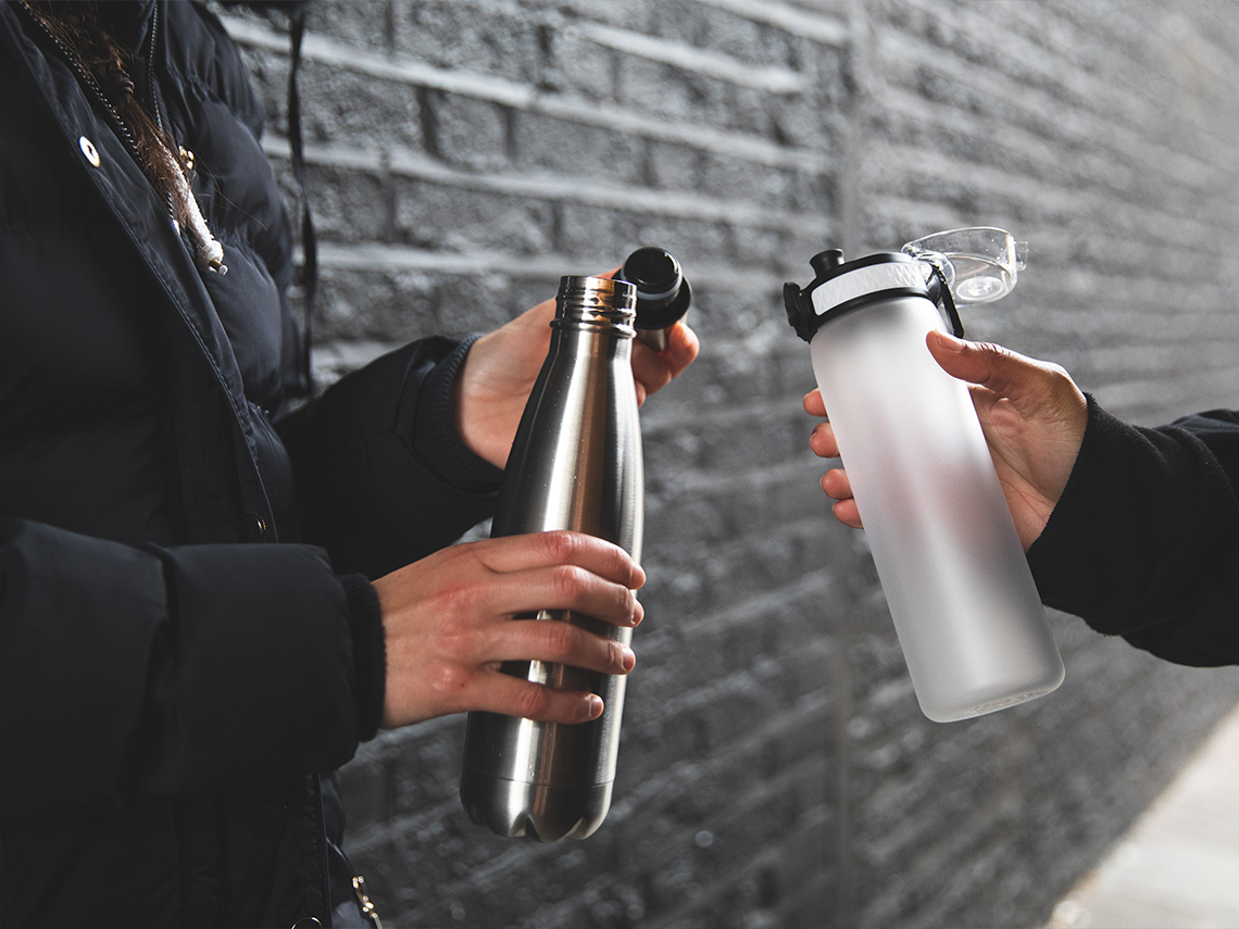 Two individuals standing across from each other holding two reusable water bottles.