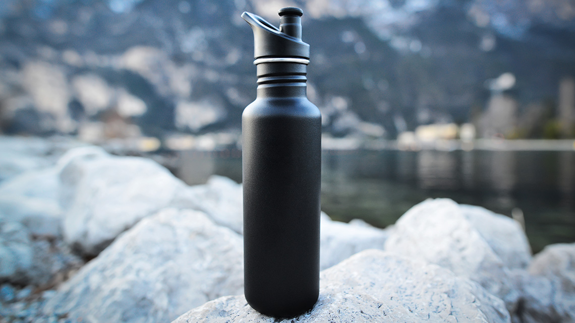 Black reusable water bottle sitting on top of a large stone.