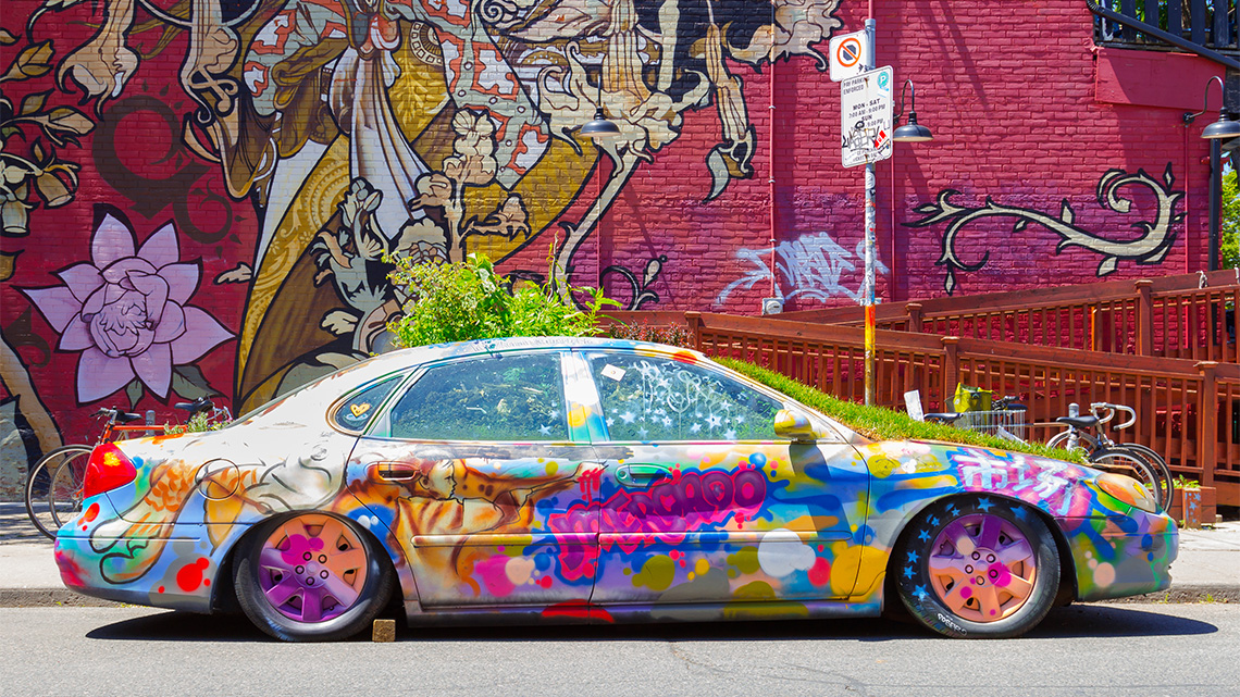 A graffitied car with plants growing out of the hood, roof, and trunk.