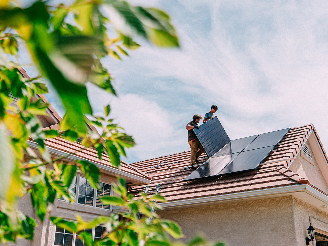 Two people installing solar panels on the roof of a house.