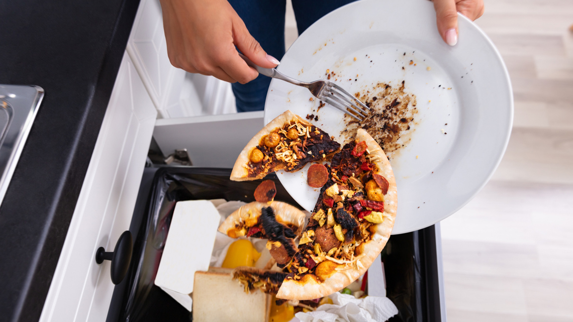 A set of hands throwing out leftovers in the garbage.