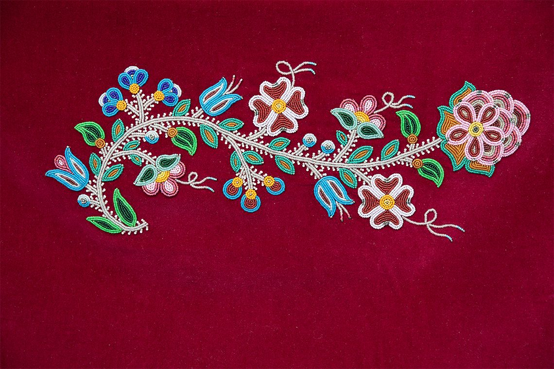 An abstract Métis beadwork art piece that looks like a vine with many types of flowers growing on it. 
