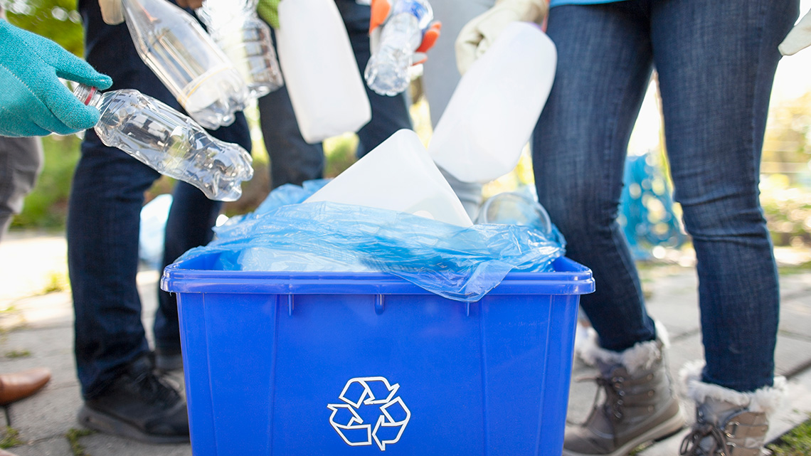 Group of volunteers cleaning up recycled bottles and placing them in a recycling bin.