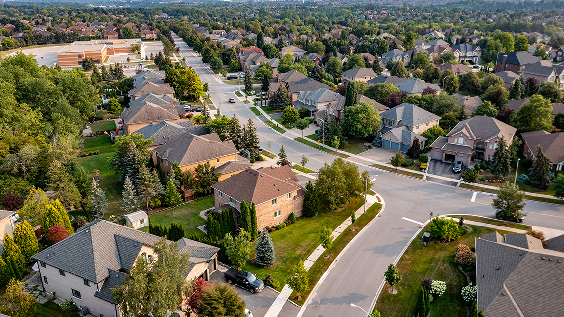 Residential street with houses, buildings, and green spaces.