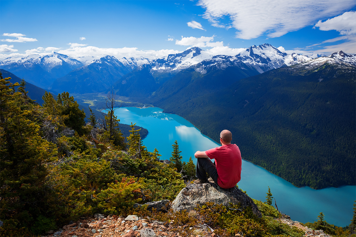 A person sitting on top of a mountain looking at the water below.