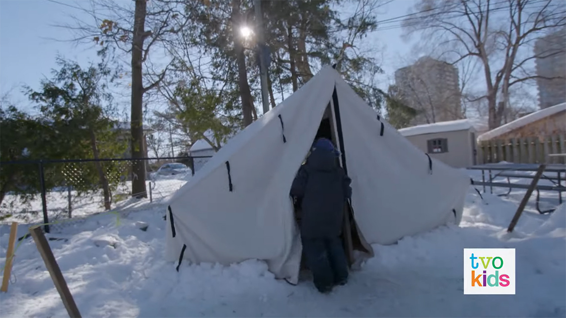 Simon is going inside a tent. The tent is set up on a snowy day.
