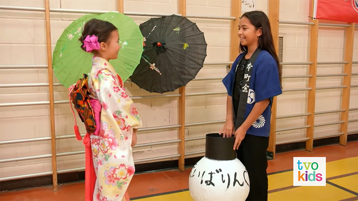 Two learners are dressed in ceremonial clothes. They have decorated with paper umbrellas and a large paper lantern.