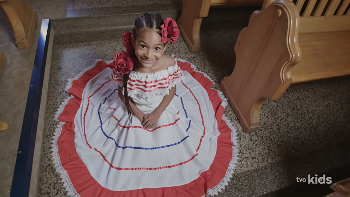 Valexia’s dress is a white ruffled dress with a wide red stripe, red and blue ribbons, and white lace edges.
