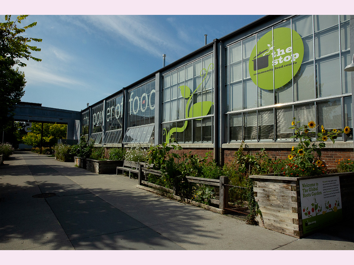 A large community greenhouse with urban gardening plots full of plants outside.