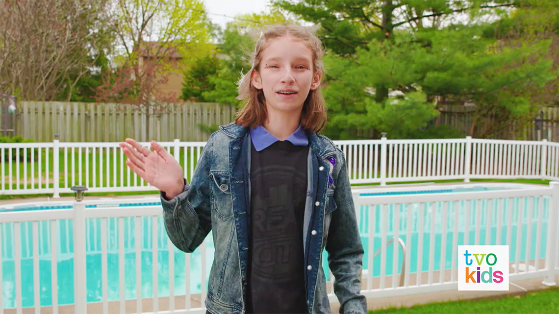 Emily waves to the camera and says, 'Shèkon.'