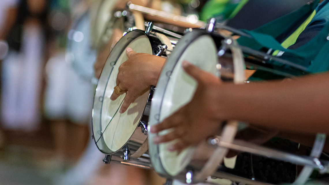 Musicians holding their cuica drums, playing with one hand outside of the drum and their other hand inside the drum on the drum stick.