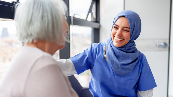 A young women wearing a hijab and speaking to a patient.