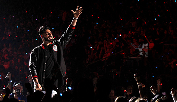 Wali Shah raising his hand and speaking into a headset microphone in an arena full of people