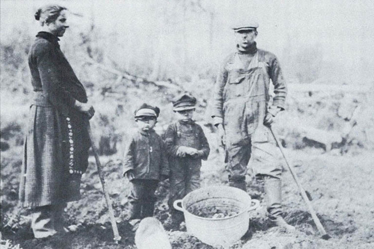 Black and white photograph of a pregnant Western Canadian woman and her family standing around a tub of potatoes in a farm field