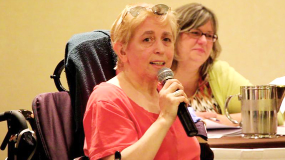 A photograph of Maria Barile speaking with a microphone.