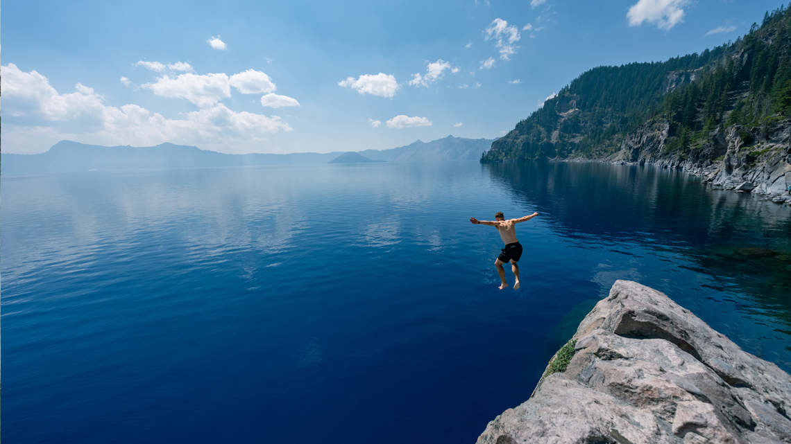 A person jumping off a cliff into a lake