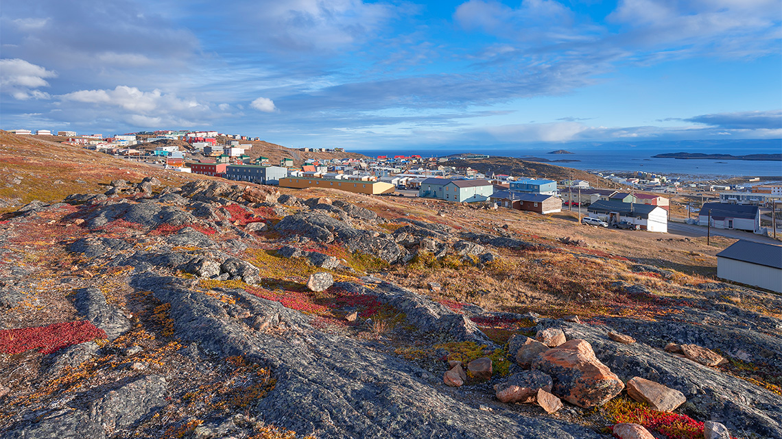 Arctic community in Canada with houses spread across the landscape, surrounded by hills and a lake.