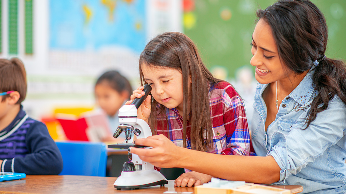 Student looking through a microscope with the support of a teacher.