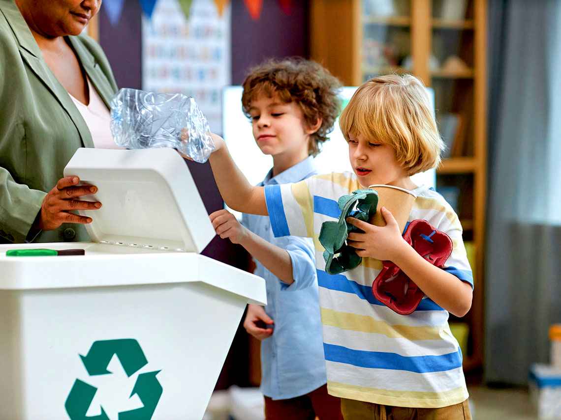 Students sorting plastic and paper into recycling bins in the classroom.