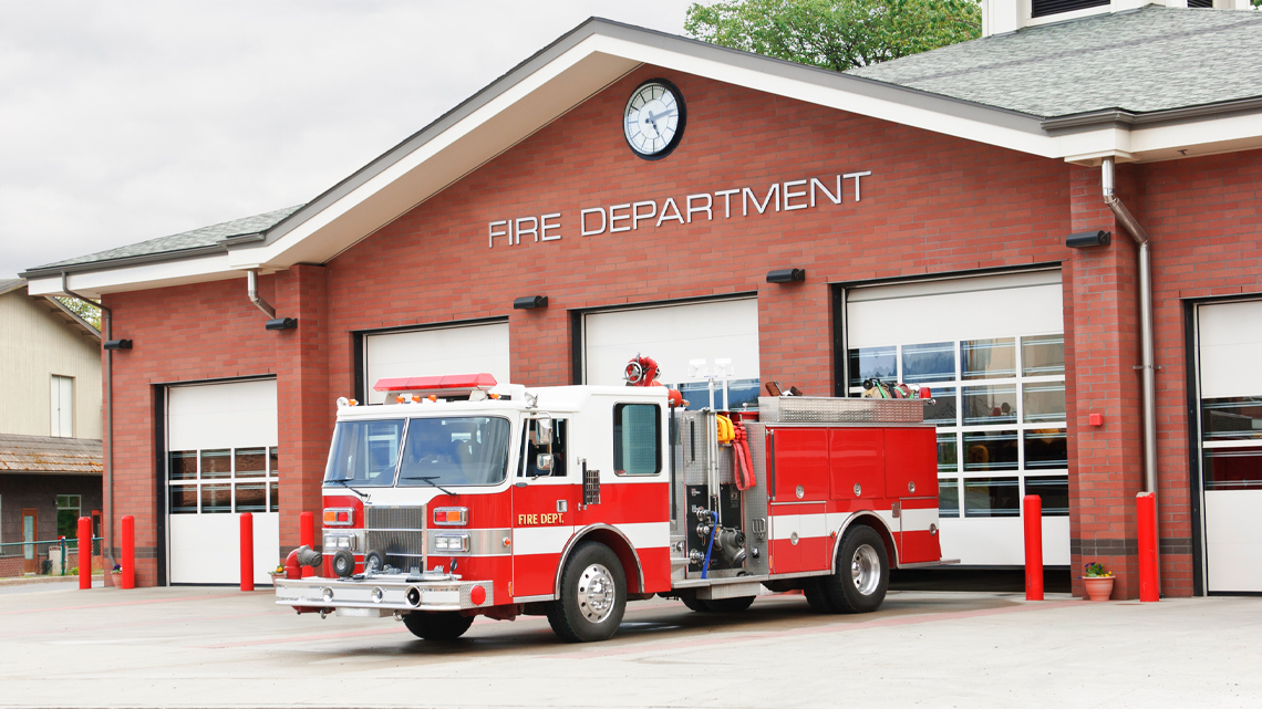 The outside of a fire station: A red brick building with a firetruck parked outside of the bay doors.