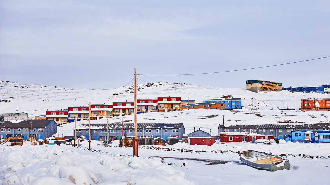 A community with several rows of identical, attached, multifamily homes near a snow-covered hill. There is a small boat in the foreground