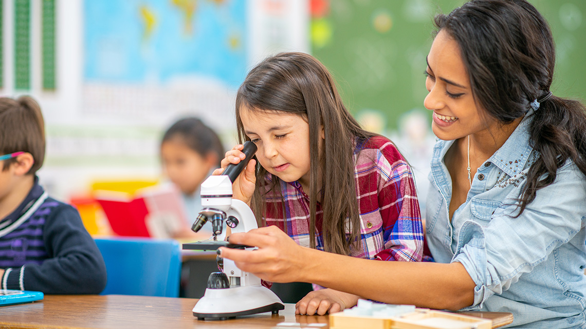 Student looking through a microscope with the support of a teacher.