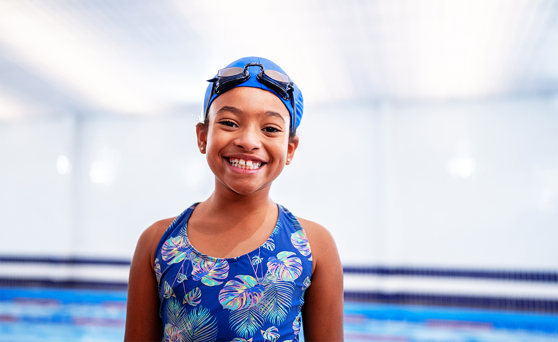 Smiling child in bathing suit beside a pool.