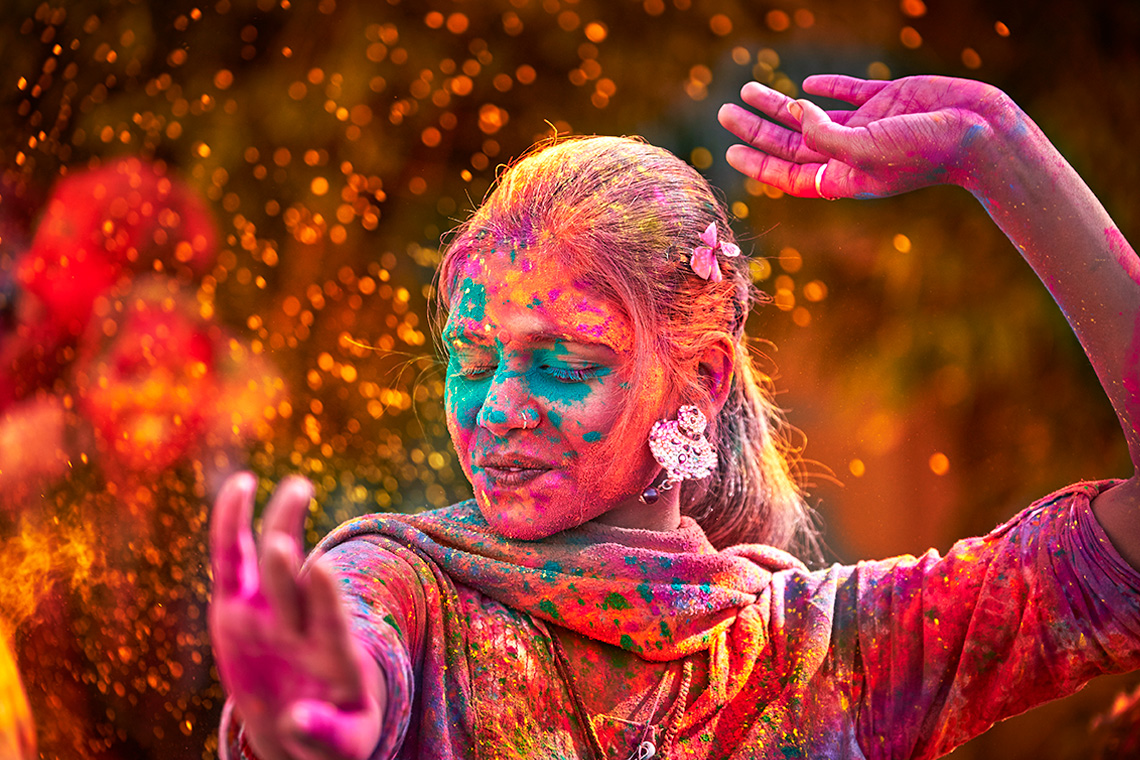 Dancer with brightly coloured powder splashed on her face, arms, and clothing.