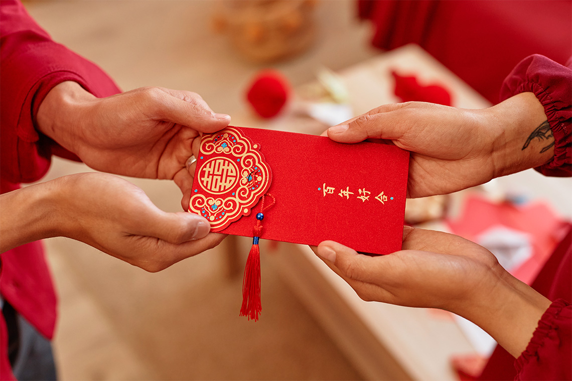 Someone passing a fancy red envelope to someone else. The envelope has Chinese characters on it