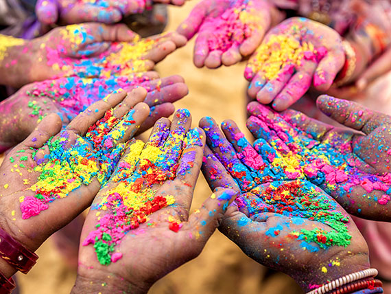 Many upturned palms covered in brightly coloured powder.
