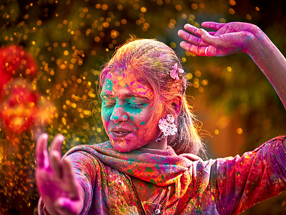 Dancer with brightly coloured powder splashed on her face, arms, and clothing.