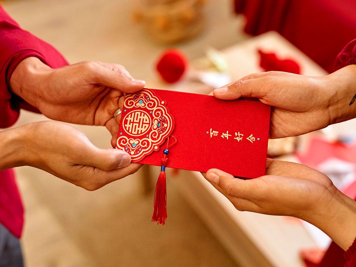 Someone passing a fancy red envelope to someone else. The envelope has Chinese characters on it