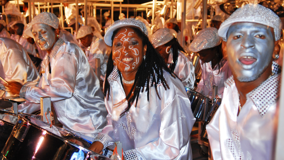 A band plays steel drums in silver clothes and silver face paint.