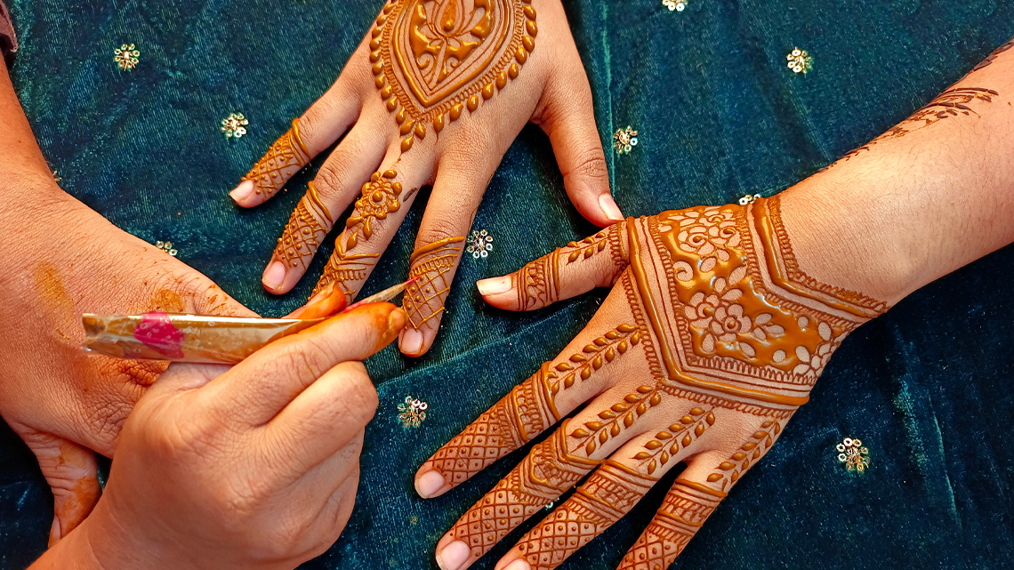 An artist applies intricate geometric and organic designs to someone's hands using henna.