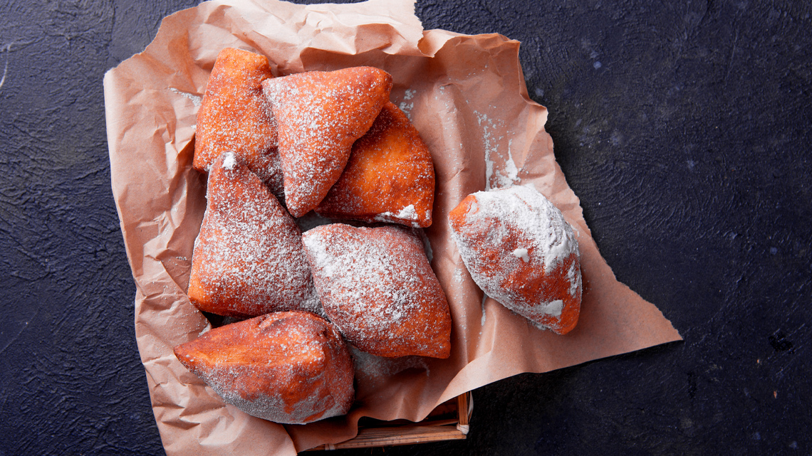 A bag full of triangular donuts dusted in icing sugar.
