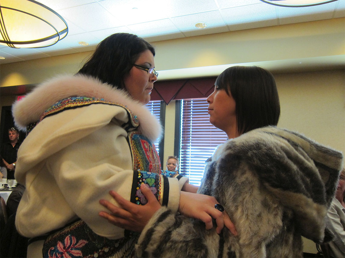Two Inuit throat singers are facing each other, holding each other’s arms, and singing together.