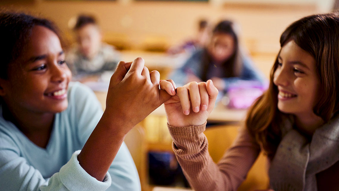 Two students making a pinky promise by linking their pinky fingers together.