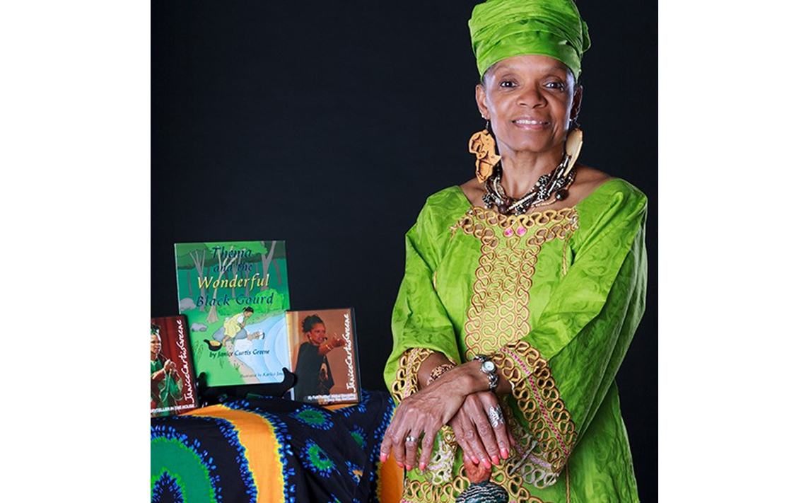 Janice Curtis Greene, a American Griot, sitting beside a table of books.