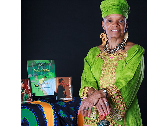 Janice Curtis Greene, a American Griot, sitting beside a table of books.