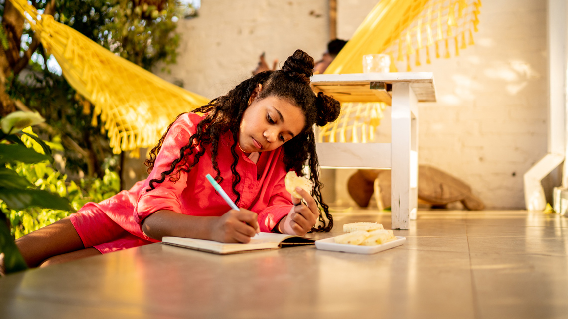 A person sits on the floor, writing in a journal.