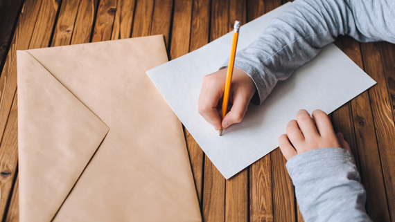 A person writing a letter beside an envelope.